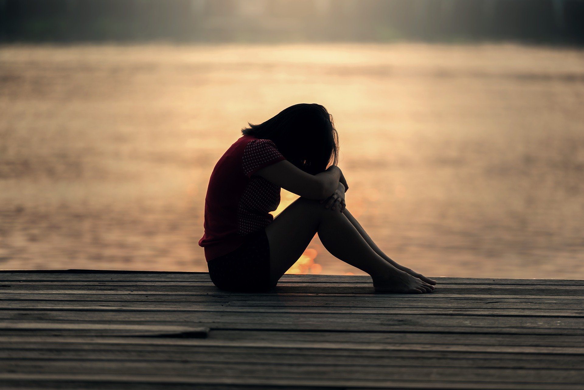girl sitting on a dock with her arms wrapped around her knees with her head down