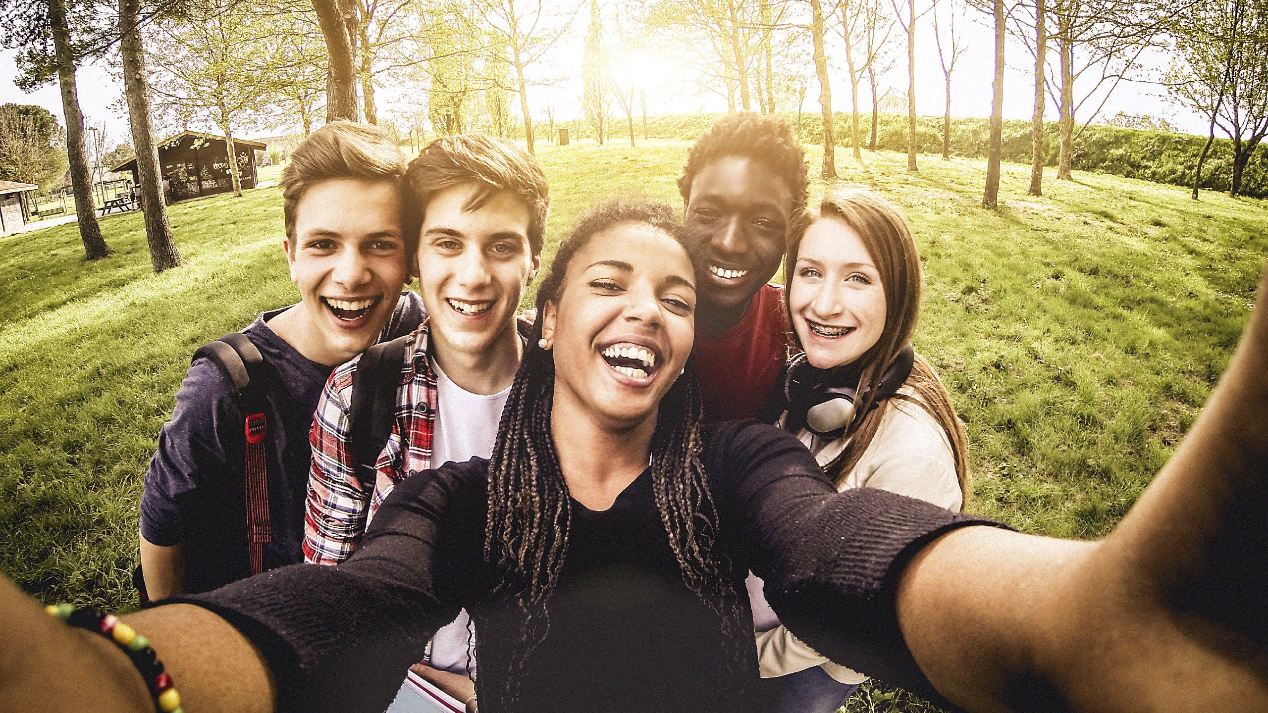 Image is a photo of 5 adolescents, smiling outdoors, holding a globe
