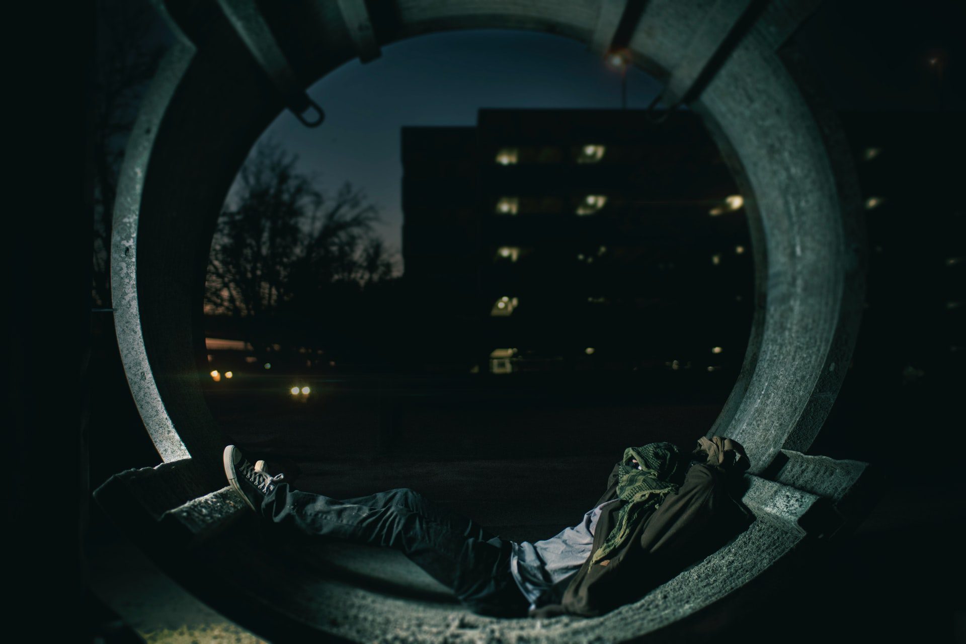 person laying inside drain pipe with building in the background