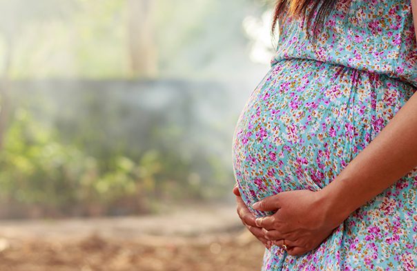 woman wearing a floral print dress cradling pregnant belly